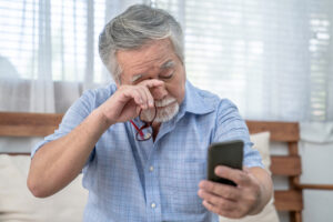 older man using phone and rubbing his eye
